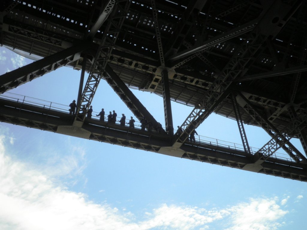 An HBM inspection team working on the steel underside of a bridge, set against an open sky
