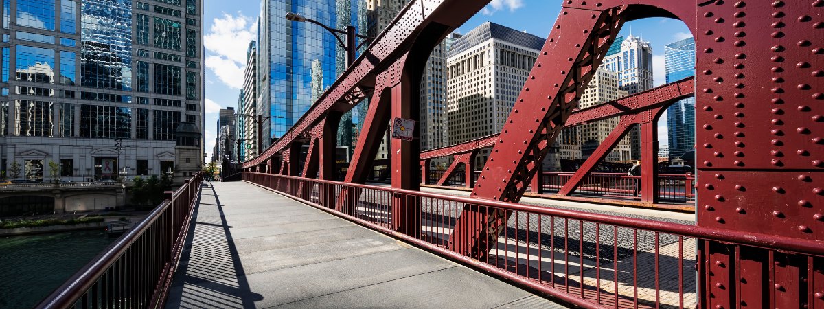 A Chicago bascule-bridge walkway, red steel trusses and the downtown skyline beyond — the urban fabric HBM engineers