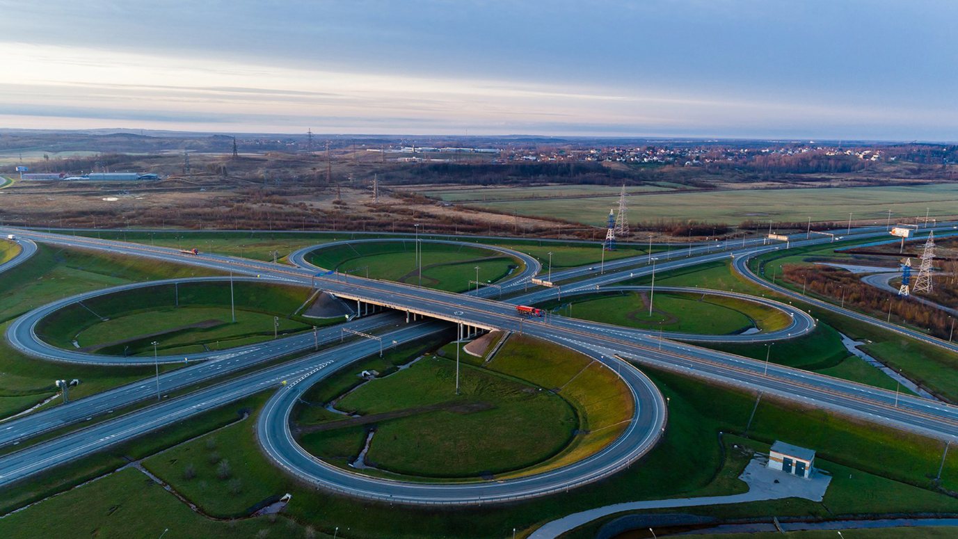 Aerial view of a cloverleaf highway interchange at dusk, lanes sweeping through green embankments
